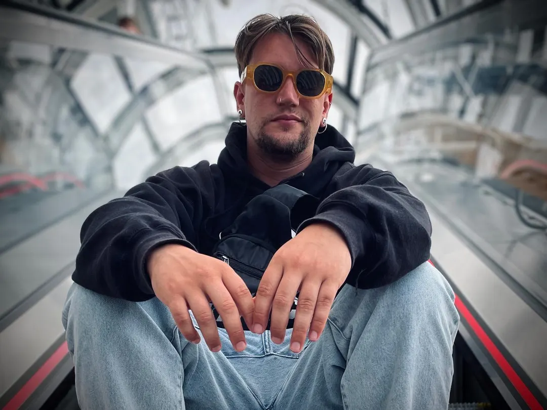 Cedecé sentado en las escaleras acristaladas del Centro Pompidou, con sudadera negra y gafas de sol redondas.