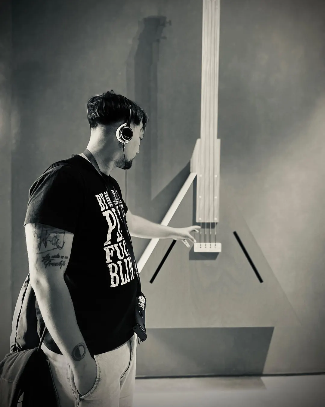 Cedecé de perfil y en blanco y negro, con auriculares de diadema, tocando una escultura sonora en la Cité de la Musique de París.